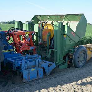 Achter de trekker hangt een bontgekleurd treintje van een Rabe kopeg (blauw), een oude vierrijige Hassia pootmachine (groen) en een oude maïszaaimachine van Kleine (geel).