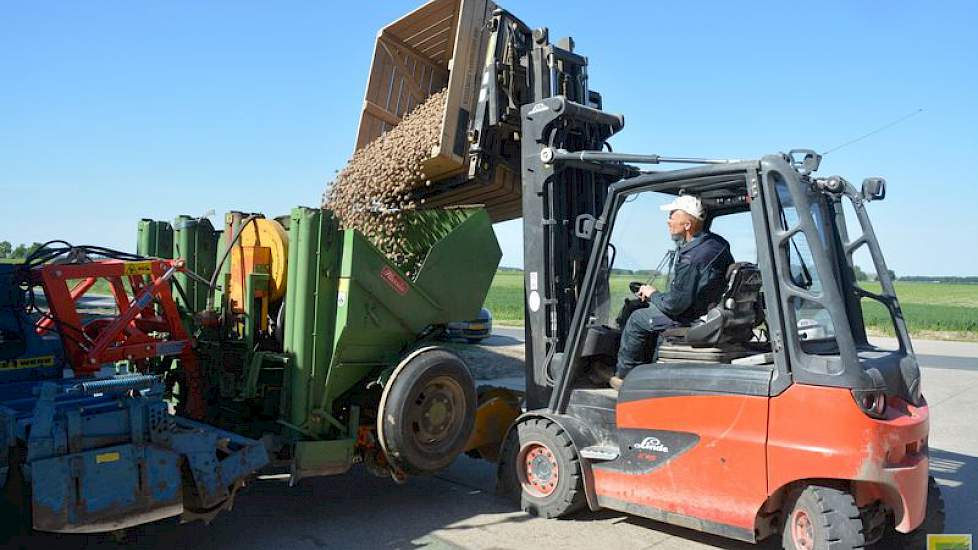 De zon schijnt fel als Westerdijk een tonskist met aardappelen leegstort in de pootcombinatie die op het erf staat.