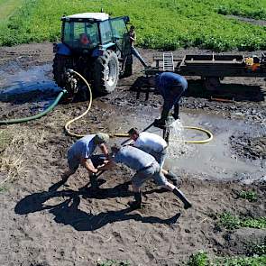 Terwijl één man van boven het water in het binnenste van de buis spuit, draaien de anderen de nieuw geplaatste pijp met behulp van metalen stang de grond in. Bas: „Bovenop de nieuwe buis zit een houten klos en daaraan is de stang bevestigd.” Daarna is het